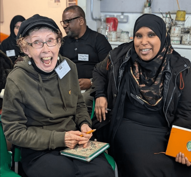 Two women at a meeting, smiling at the camera.